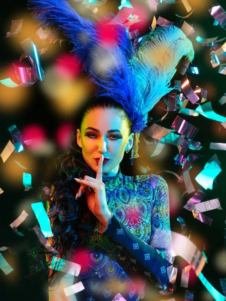 Beautiful young woman in carnival and masquerade costume in colorful neon lights on black background in flying confetti — Stock Photo, Image