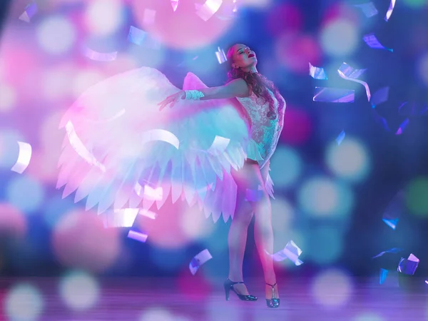 Mladá žena tanečnice s anděly křídla v neonovém světle na černém pozadí v létání konfety — Stock fotografie