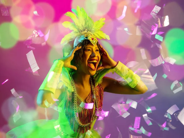 Mooie jonge vrouw in carnaval en maskerade kostuum in kleurrijke neon lichten op gradiënt achtergrond in vliegende confetti — Stockfoto