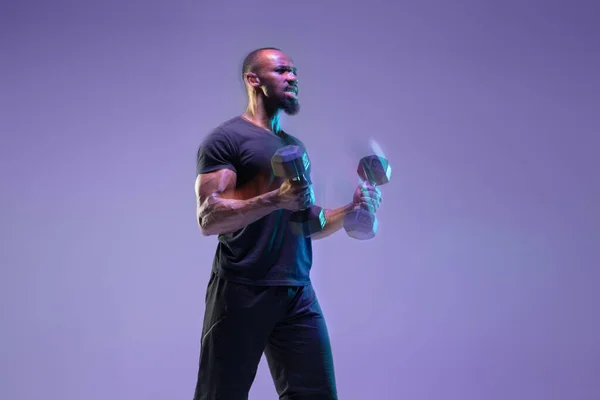Junger afrikanisch-amerikanischer Bodybuilder beim Training vor lila Hintergrund in neon, gemischtem Licht — Stockfoto