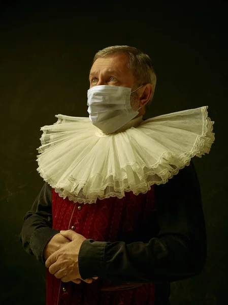 Homem sênior como um cavaleiro medieval em fundo escuro usando máscara protetora contra coronavírus — Fotografia de Stock