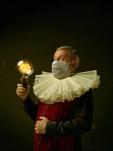 Homem sênior como um cavaleiro medieval em fundo escuro usando máscara protetora contra coronavírus — Fotografia de Stock