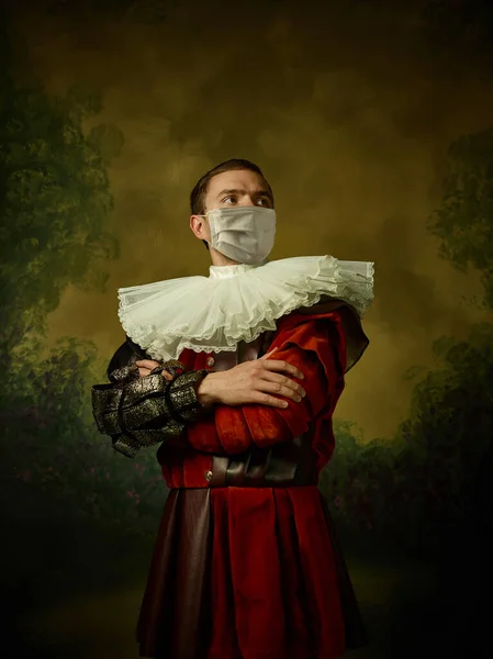 Ung man som en medeltida riddare på mörk bakgrund bär skyddande mask mot coronavirus — Stockfoto