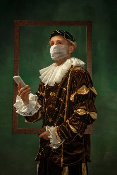 Ung man som en medeltida riddare på mörk bakgrund bär skyddande mask mot coronavirus — Stockfoto