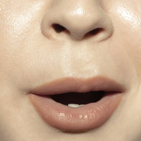 Close-up female mouth with natural nude gloss lips make-up. Cosmetology, dentistry and beauty care, emotions