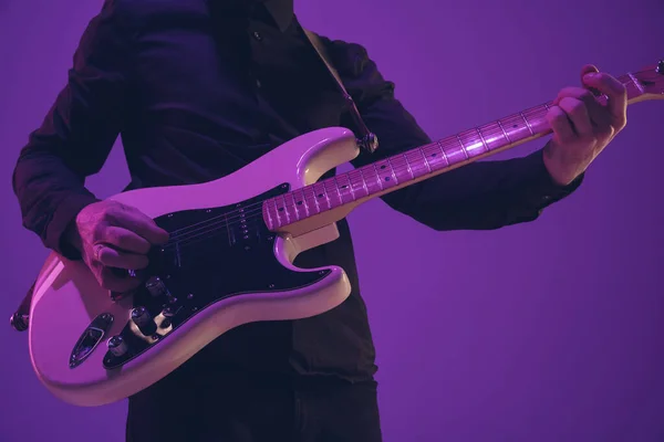 Joven músico caucásico tocando la guitarra en luz de neón sobre fondo púrpura — Foto de Stock