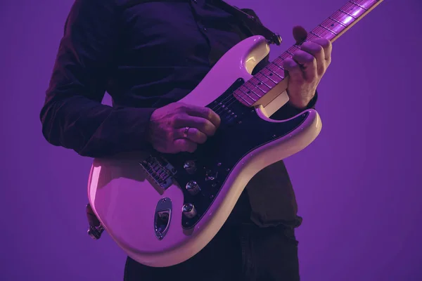 Jovem músico caucasiano tocando guitarra em luz de néon em fundo roxo — Fotografia de Stock