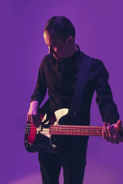 Joven músico caucásico tocando la guitarra en luz de neón sobre fondo púrpura — Foto de Stock