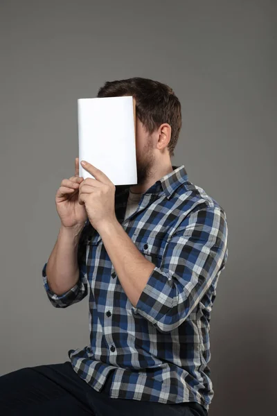 Щасливий день світової книги, читати, щоб стати кимось іншим - людина прикриває обличчя книгою, читаючи на сірому фоні — стокове фото