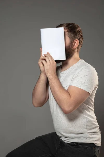 Feliz día mundial del libro, leer para convertirse en otra persona - hombre cubriendo la cara con el libro mientras lee sobre fondo gris — Foto de Stock