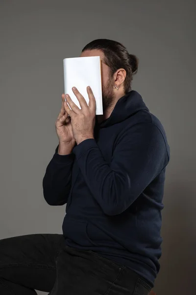 Happy World Book Day, gelesen, um jemand anderes zu werden - Mann bedeckt Gesicht mit Buch, während er auf grauem Hintergrund liest — Stockfoto