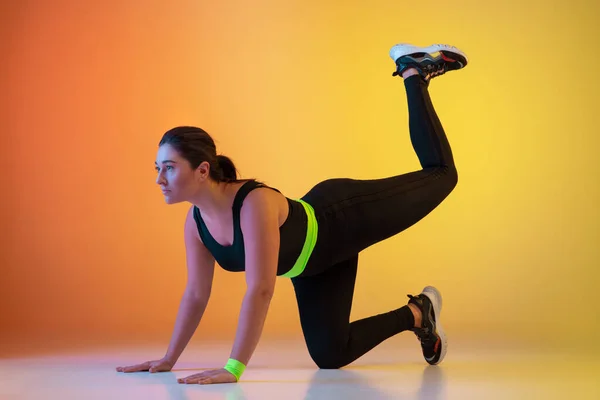 Young caucasian plus size female models training on gradient orange background — Stock Photo, Image