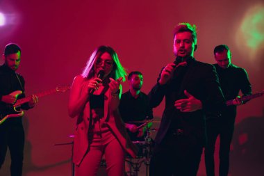 Kafkasyalı genç müzisyenler, kırmızı stüdyo arka planında neon ışıkta performans sergiliyorlar.