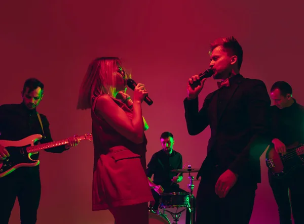 Junge kaukasische Musiker, Band tritt im Neonlicht auf rotem Studiohintergrund auf — Stockfoto