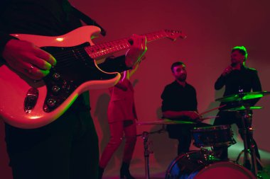 Kafkasyalı genç müzisyenler, kırmızı stüdyo arka planında neon ışıkta performans sergiliyorlar.