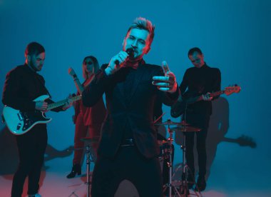 Kafkasyalı genç müzisyenler, mavi stüdyo arka planında neon ışığı altında şarkı söyleyen orkestra, öndeki şarkıcı.