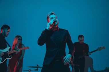 Kafkasyalı genç müzisyenler, mavi stüdyo arka planında neon ışığı altında şarkı söyleyen orkestra, öndeki şarkıcı.