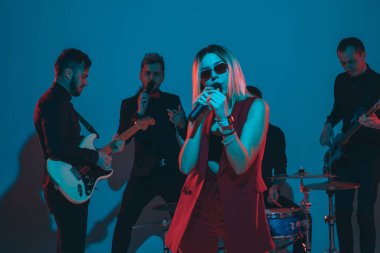 Kafkasyalı genç müzisyenler, mavi stüdyo arka planında neon ışığı altında şarkı söyleyen orkestra, öndeki şarkıcı.