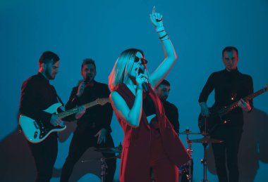 Kafkasyalı genç müzisyenler, mavi stüdyo arka planında neon ışığı altında şarkı söyleyen orkestra, öndeki şarkıcı.