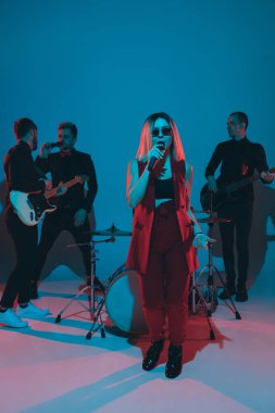Kafkasyalı genç müzisyenler, mavi stüdyo arka planında neon ışığı altında şarkı söyleyen orkestra, öndeki şarkıcı.