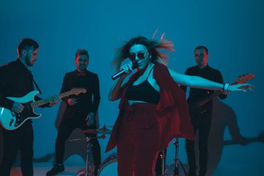 Kafkasyalı genç müzisyenler, mavi stüdyo arka planında neon ışığı altında şarkı söyleyen orkestra, öndeki şarkıcı.