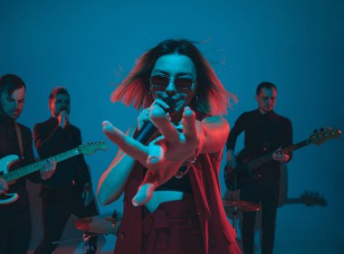 Kafkasyalı genç müzisyenler, mavi stüdyo arka planında neon ışığı altında şarkı söyleyen orkestra, öndeki şarkıcı.
