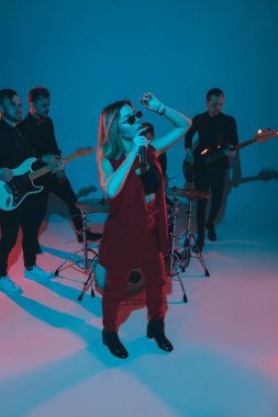 Kafkasyalı genç müzisyenler, mavi stüdyo arka planında neon ışığı altında şarkı söyleyen orkestra, öndeki şarkıcı.
