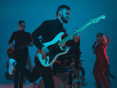 Kafkasyalı genç müzisyenler, mavi stüdyo arka planında neon ışıkta çalan grup, önde gitarist