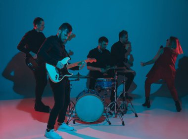 Kafkasyalı genç müzisyenler, mavi stüdyo arka planında neon ışıkta çalan grup, önde gitarist