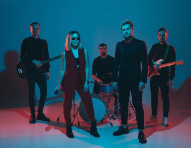 Genç Kafkasyalı müzisyenler, mavi stüdyo arka planında neon ışıkta performans sergiliyorlar.