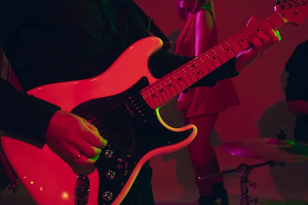 Young caucasian musician, band performing in neon light on red studio background