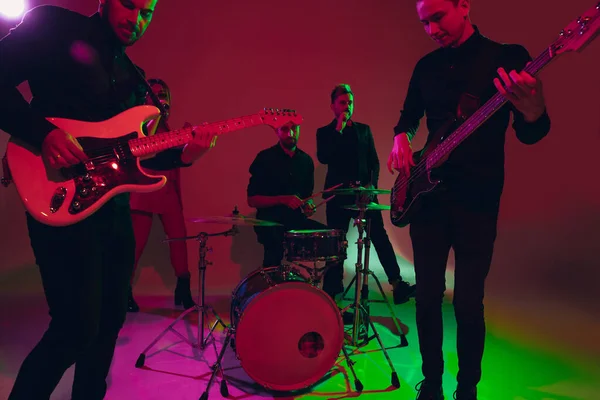 Junge kaukasische Musiker, Band tritt im Neonlicht auf rotem Studiohintergrund auf — Stockfoto