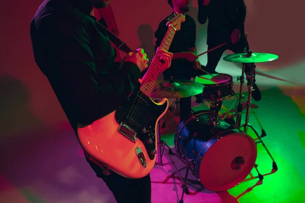 Young caucasian musician, band performing in neon light on red studio background