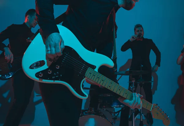 Junge kaukasische Musiker, Band spielt im Neonlicht auf blauem Studiohintergrund, Gitarrist vorn — Stockfoto