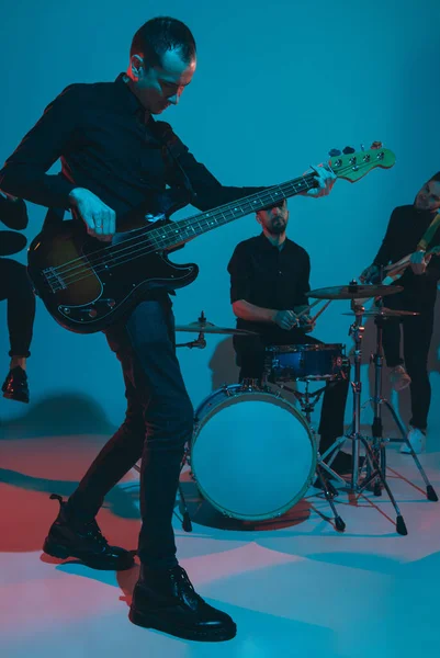 Jovens músicos caucasianos, banda se apresentando em luz de néon no fundo do estúdio azul, guitarrista na frente — Fotografia de Stock