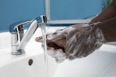 Adam banyoda ellerini dikkatlice yıkıyor. Enfeksiyon ve zatürree virüsünün yayılmasını önlemek