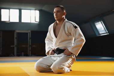 Kimonolu genç judo dövüşçüsü spor salonunda kendine güvenen, güçlü ve sağlıklı.