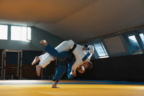 Dos jóvenes luchadores de judo en kimono entrenando artes marciales en el gimnasio con expresión, en acción y movimiento —  Fotos de Stock