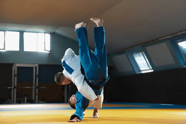 Két fiatal judo harcos kimonóban harcművészetet edz a tornateremben, kifejezéssel, akcióban és mozgásban. — Stock Fotó