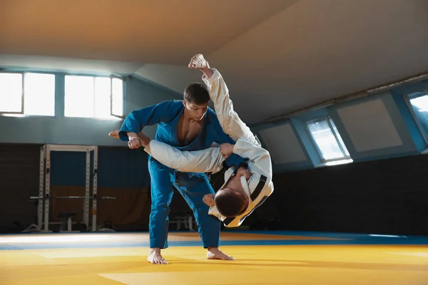 Két fiatal judo harcos kimonóban harcművészetet edz a tornateremben, kifejezéssel, akcióban és mozgásban. — Stock Fotó