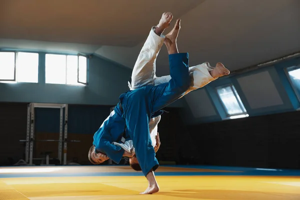 Dos jóvenes luchadores de judo en kimono entrenando artes marciales en el gimnasio con expresión, en acción y movimiento — Foto de Stock
