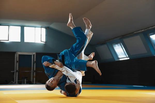 Két fiatal judo harcos kimonóban harcművészetet edz a tornateremben, kifejezéssel, akcióban és mozgásban. — Stock Fotó