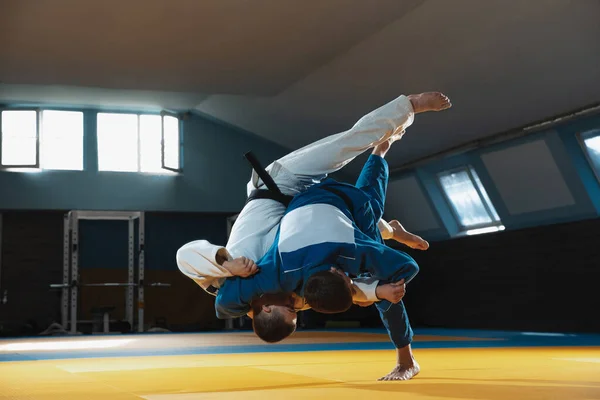 Dois jovens lutadores de judô em kimono treinando artes marciais no ginásio com expressão, em ação e movimento — Fotografia de Stock