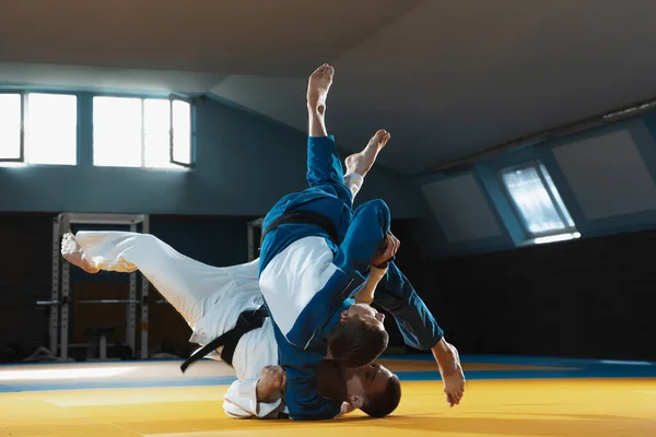 Dos jóvenes luchadores de judo en kimono entrenando artes marciales en el gimnasio con expresión, en acción y movimiento — Foto de Stock