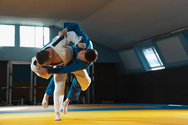 Két fiatal judo harcos kimonóban harcművészetet edz a tornateremben, kifejezéssel, akcióban és mozgásban. — Stock Fotó