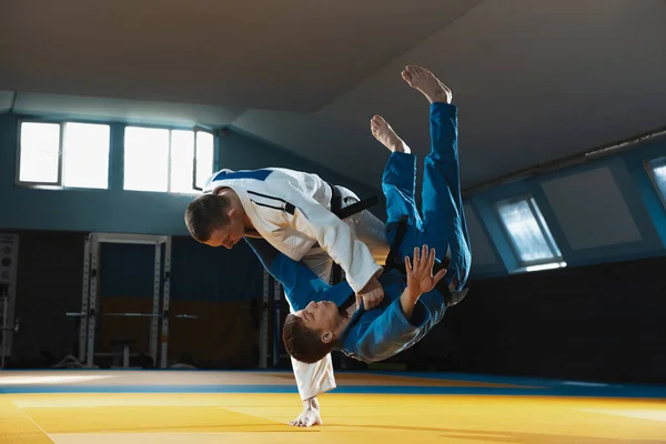 Két fiatal judo harcos kimonóban harcművészetet edz a tornateremben, kifejezéssel, akcióban és mozgásban. — Stock Fotó