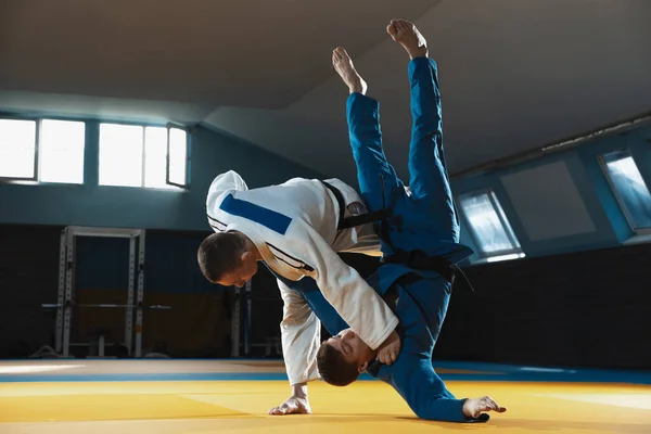 Dos jóvenes luchadores de judo en kimono entrenando artes marciales en el gimnasio con expresión, en acción y movimiento — Foto de Stock