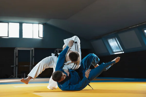 Deux jeunes combattants de judo en kimono s'entraînent aux arts martiaux dans le gymnase avec expression, action et mouvement — Photo