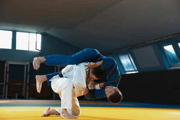 Twee jonge judo vechters in kimono trainen martial arts in de sportschool met expressie, in actie en beweging — Stockfoto