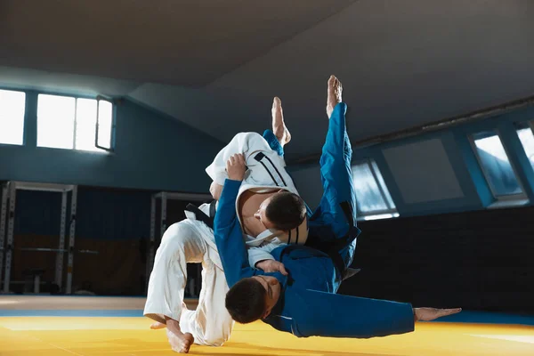 Dos jóvenes luchadores de judo en kimono entrenando artes marciales en el gimnasio con expresión, en acción y movimiento — Foto de Stock